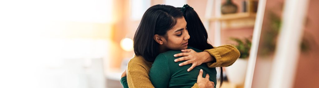 A joyous Indian family sharing a warm hug and reuniting safely at the airport after booking affordable Gaura Travel flights.